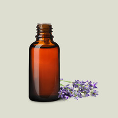 Bottle of lavender essential oil and flowers on light background