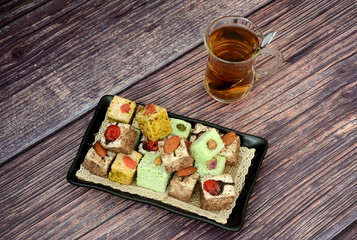 A plate with a variety of Turkish sweets and a cup of hot tea on a dark wooden table.
