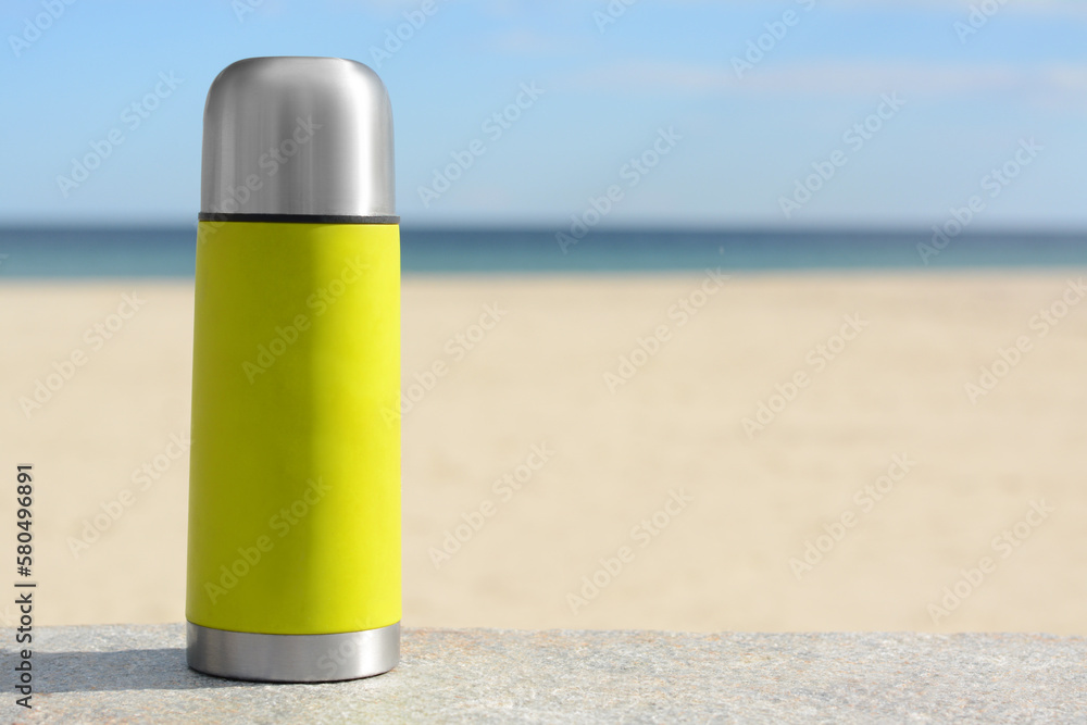 Sticker Metallic thermos with hot drink on stone surface near sea, space for text