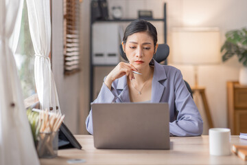 Happy Young Asian woman using laptop while working at home with documents. online documentation calculator to calculate the numbers, finance accounting office concept