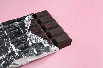 Fototapeta na wymiar Delicious dark chocolate bar wrapped in foil on pink background. Space for text