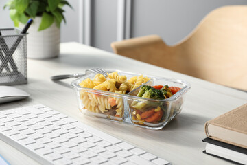 Container with tasty food, keyboard and books on white wooden table. Business lunch