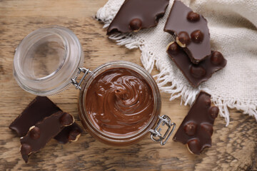 Chocolate pieces and glass jar of sweet paste on wooden table, flat lay