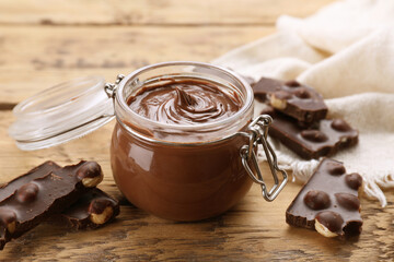 Chocolate pieces and glass jar of sweet paste on wooden table