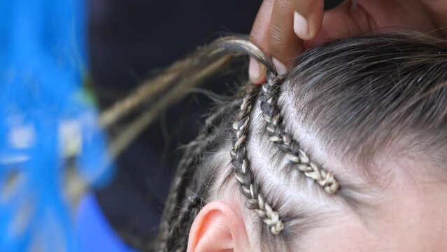 Close-up of the hands of an experienced black master tightly braiding a thin braid to a woman using artificial materials. African hairdresser weaves popular Afro-braids to a woman