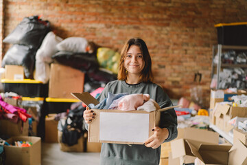 Volunteer teengirl preparing donation boxes for people. Donation clothing for refugees, support of...