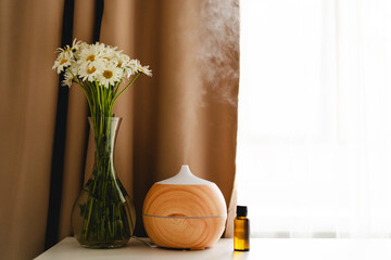 Aromatherapy concept. Aroma oil diffuser on the table against the window. Air freshener. Ultrasonic...