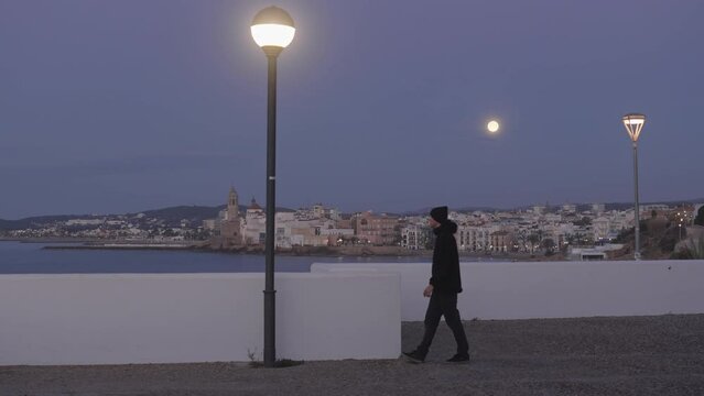 city scape, man enters, takes photos of coastal town, as moon shines above and light switches off