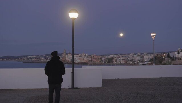 city scape, man enters, takes photos of coastal town, as moon shines above