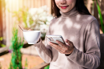 Young female with cup of coffee using mobile phone and relaxing in cafe, Modern lifestyle