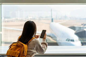 Young Asian woman traveler using smart phone while waiting for her flight at the airport - 580501671
