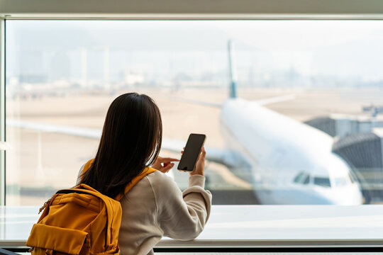 Young Asian woman traveler using smart phone while waiting for her flight at the airport