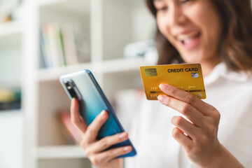 Happy young Asian woman holding credit card and using smartphone for shopping online with payment on internet banking.