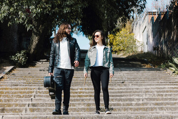 young hispanic couple man and woman in rock and roll style walking and playing guitar in the street...
