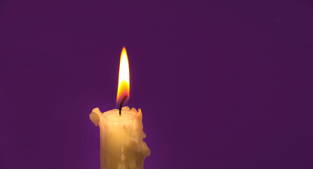 Burning wax candle in close up over purple background