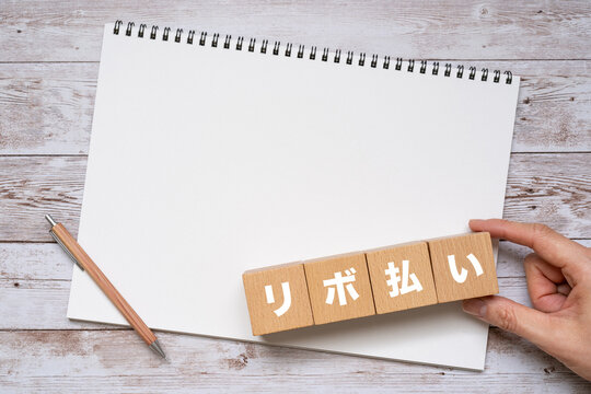 リボ払いと書かれたブロック、ノート、ペン、手