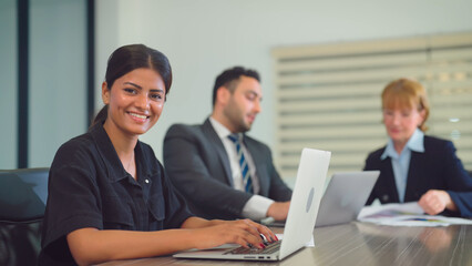 Obraz na płótnie Canvas Portrait of beautiful indian woman looking to camera with attractive smiling at office. She working at office with team. Business, Teamwork, Corporate, Lifestyle, Technology and Diversity concept.