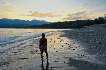 Naklejka premium Panoramic drone shot of Ende beach on Flores with a golden sunset behind hills, in the foreground a person from behind.