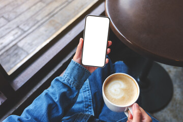 Top view mockup image of a woman holding mobile phone with blank screen and coffee cup in cafe - obrazy, fototapety, plakaty