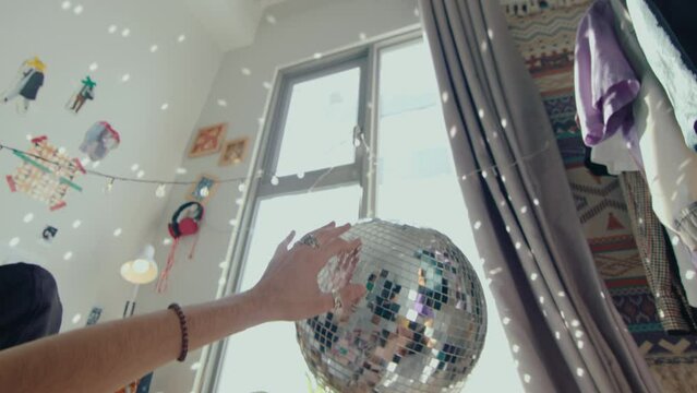 Close up shot of young man lying on bed at home during the day and turning shining disco ball in hands