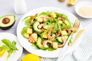 Flat lay of Healthy salad plate. Fresh seafood recipe. Grilled shrimps and fresh vegetables (avocado, arugula, mango) on gray concrete background. 