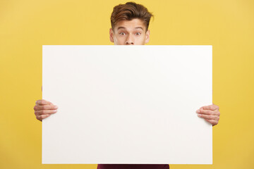 Surprised man hiding behind a blank panel