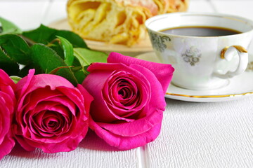 bouquet of three bud of red roses in a row close up and porcelain pattern cup of black coffee on saucer with fresh pastries sliced on blurred background