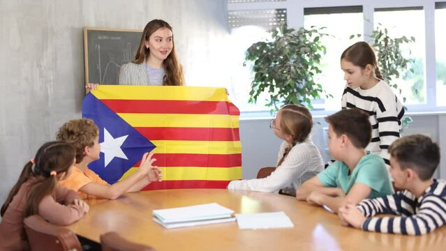 Young female teacher holding colorful flag of Estelada while working with preteens in classroom. High quality 4k footage