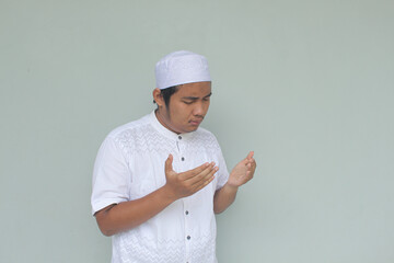 Handsome happy Asian Muslim man praying to God. Isolated on gray background