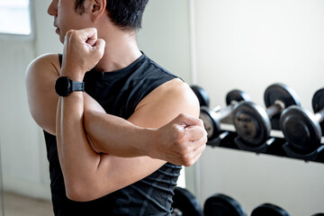 Fototapeta na wymiar Asian sport man in black sportswear stretching arms with cross-body shoulder stretch pose and warming up before weight training in fitness gym. Physical exercise posture for muscle stretching.