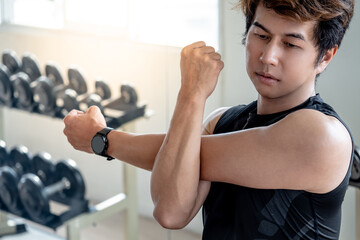 Asian sport man in black sportswear stretching arms with cross-body shoulder stretch pose and warming up before weight training in fitness gym. Physical exercise posture for muscle stretching.