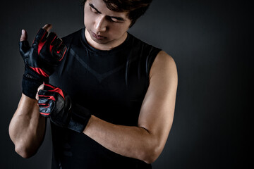 Asian sport man with well trained body in black sportswear wearing leather weight lifting gloves....