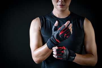 Asian sport man with well trained body in black sportswear wearing leather weight lifting gloves....