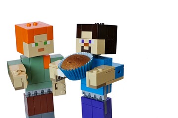 Fototapeta premium LEGO Minecraft figures o Steve and Alex, Steve holding baked brown muffin cake in blue paper cup. White background. 