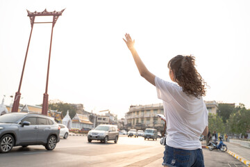 Young Asian woman with hand up calling a taxi cab on busy city street. Teenage tourist using taxi service application via smartphone - with copy space