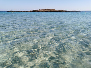 Fig Tree Bay beach, crystal clear water, white sand at the bottom, small island off the coast.