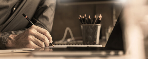 Close up man hand working of Architect sketching pencil project on blueprint at site construction work. Concept of architect, engineer in the office desk construction project banner