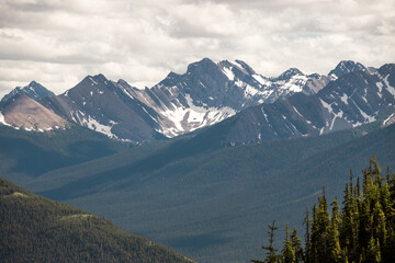 Obraz premium Scenic alpine landscape with great mountain under cloudy sky. Beautiful mountain scenery with big sharp rocks in cloudy sky above coniferous forest. Awesome Rocky mountains