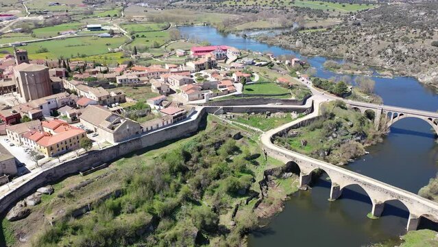 Scenic drone view of historic center of Ledesma town on banks of Tormes river surrounded by ancient defensive wall on sunny spring day on background of large natural rural landscape, Salamanca, Spain