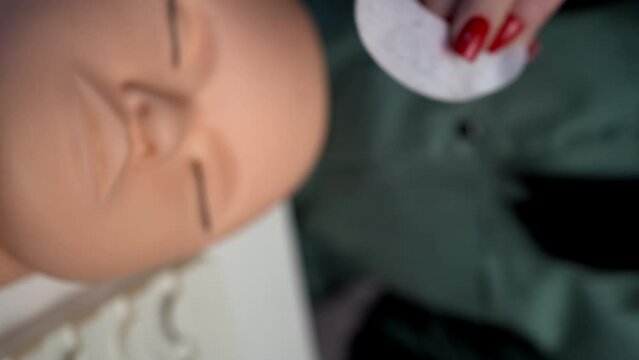 A beauty mannequin training head with a person practicing lash extension techniques. Female hands preparing glue cotton tape under eye. Basic training to build eyelashes.