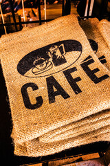 A stack of empty tan jute coffee sacks with ' Cafe ' printed in black and a coffee symbol.