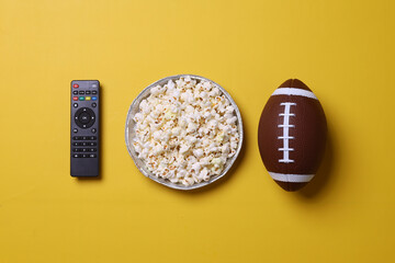 A bowl of popcorn, remote control and rugby ball. A classic set of sports fans on yellow background.