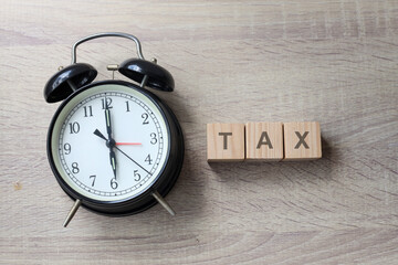 The word tax on wooden cubes with an alarm clock on wooden background. Tax payment reminder or annual taxation concept.