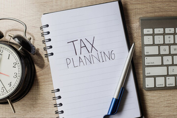 Overhead view of work desk with keyboard, pen, notebook and alarm clock. Tax Planning written on...