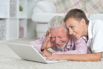 Grandfather with grandson using laptop while lying on floor