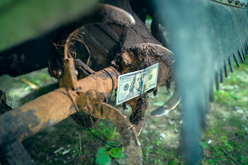 Stopped rural industry due to financial problems. A hundred dollar bill close-up on the teeth of a tractor rototiller. Repair and maintenance of agricultural machinery. Payment for services