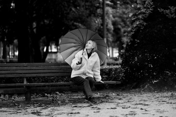 A woman sits on a park bench in rainy weather. Black and white photo.