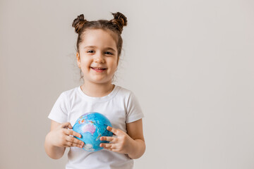 a happy little girl is holding a small globe planet in her hands in a white T-shirt on a white background. Earth Day, space for text