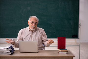 Old male teacher in front of green board