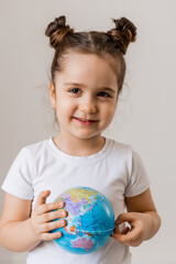 a happy little girl is holding a small globe planet in her hands in a white T-shirt on a white background. Earth Day, space for text